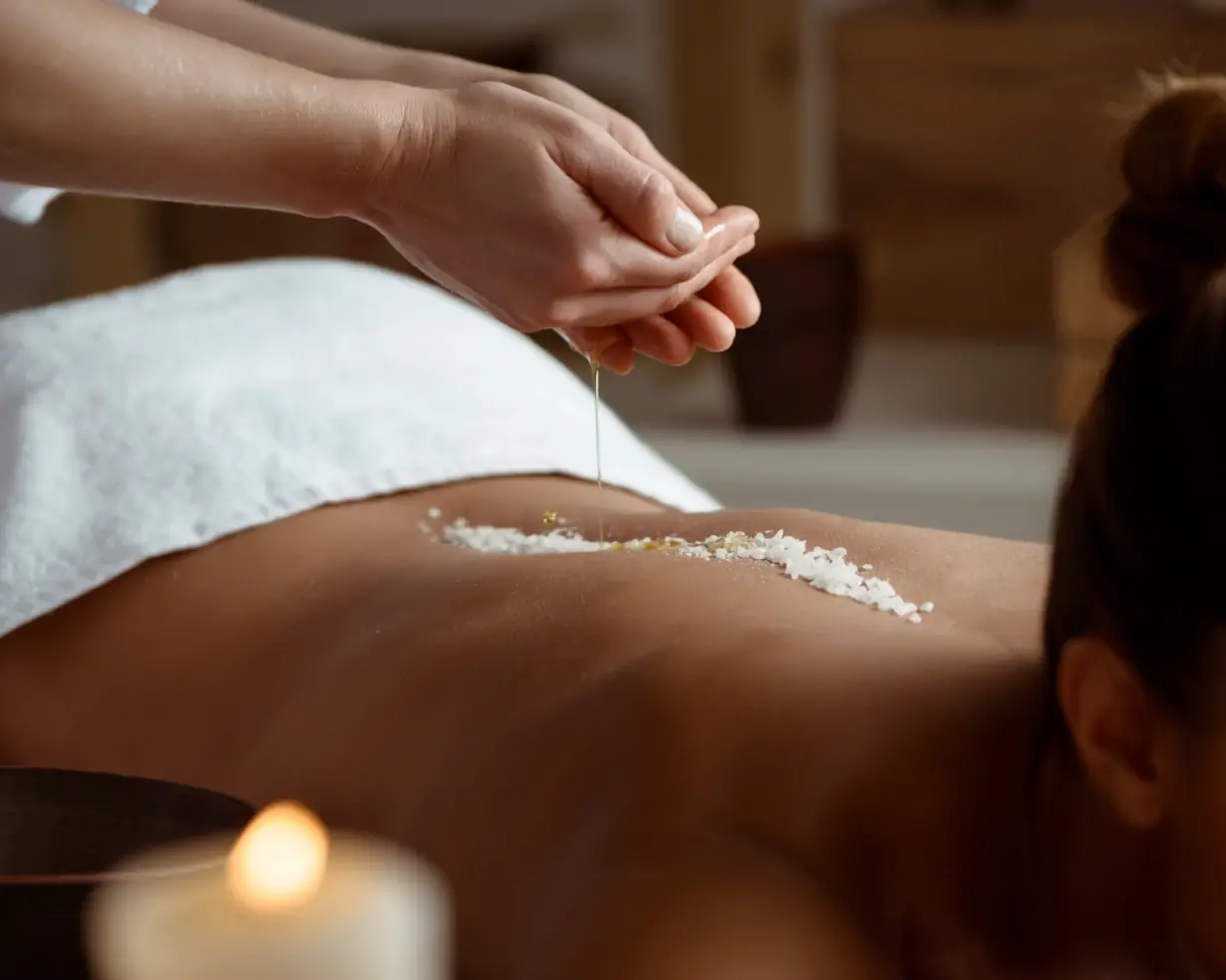 Natural body scrub with sea salt and herbs in a small ceramic bowl with a wooden spoon